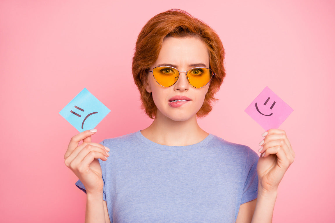 A woman holding a sad and happy face card, symbolizing mood swings in females and emotional balance.